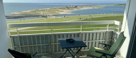 A balcony with two chairs and a small table, overlooking a coastal area with a beach and water.