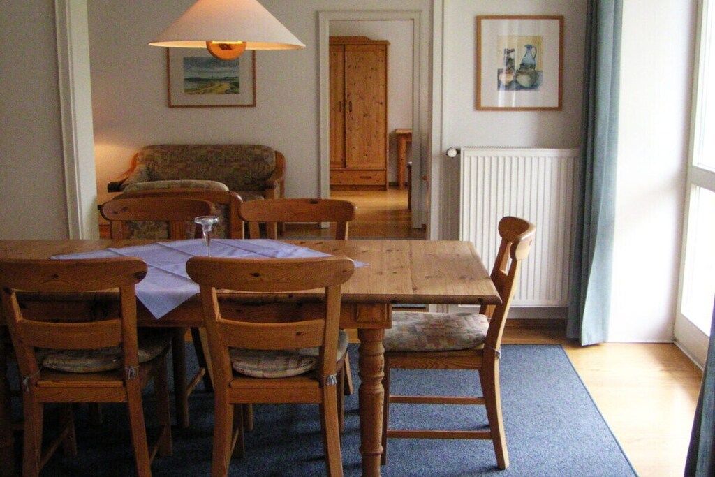 Een eetgedeelte met een houten tafel en stoelen, een lamp, een bank en een kast op de achtergrond.