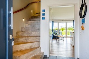 Eine Treppe führt zu einem Raum mit Blick ins Freie, einem Essbereich mit Tisch und Stühlen sowie einem wandmontierten Spiegel.