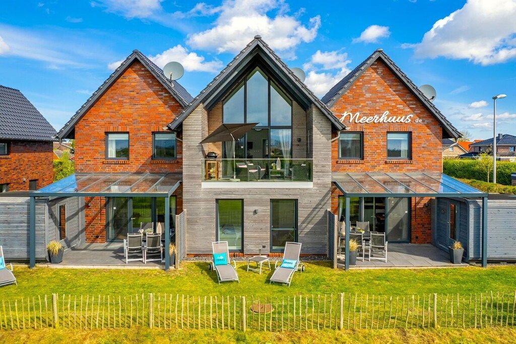 Een modern herenhuis met twee verdiepingen, een glazen conservatorium, een herkenbaar naam 'Neerhuis' en een keurig onderhouden gazon.