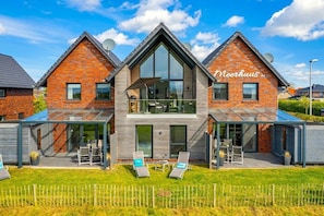 Ein modernes, zweistöckiges Haus mit Wintergarten, einem sichtbaren Namen 'Neerhuis' und einem gepflegten Rasen.