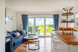 A modern living space with a sofa, a coffee table, and a dining area with a fruit display. - Meerhuus Carolinensiel House 3 (Carolinensiel)
