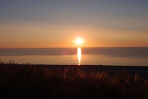 Ein Sonnenuntergang über ruhigem Wasser, im Vordergrund eine Silhouette von Gras.