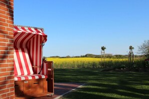 Eine Terrasse mit einer rot-weiß gestreiften Markise, einer Holzbank und Blick auf ein gelbes Feld.
