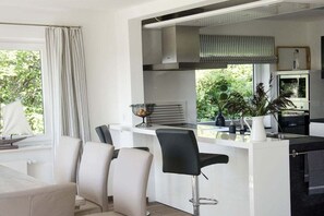 Eine moderne Küche mit einer zentralen Kochinsel, Barhocker und Blick auf Grünflächen.