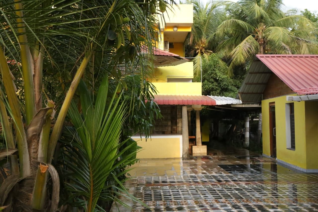 A yellow building with a tiled floor, surrounded by palm trees and greenery.