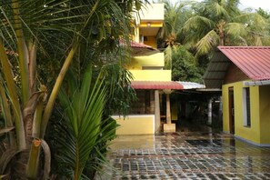 A yellow building with a tiled floor, surrounded by palm trees and greenery.