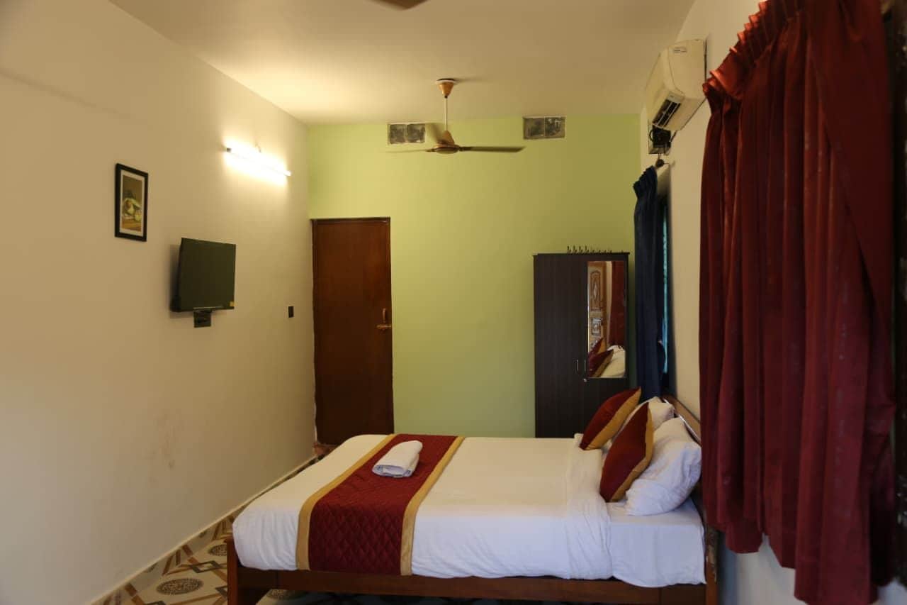 A hotel room with a bed, a ceiling fan, a wardrobe, and a door.