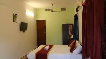 A hotel room with a bed, a ceiling fan, a wardrobe, and a door.
