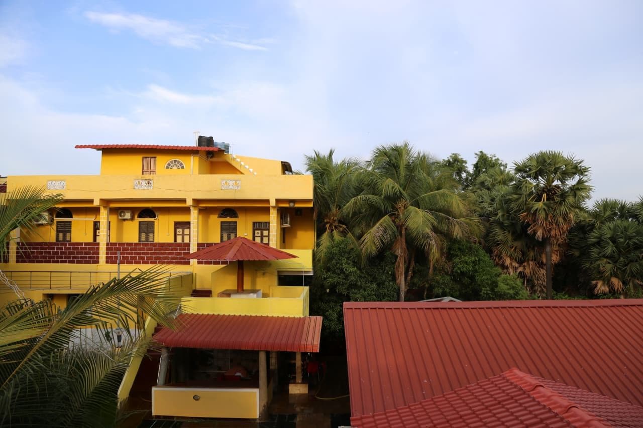 A yellow building with multiple windows and a red roof, surrounded by palm trees.