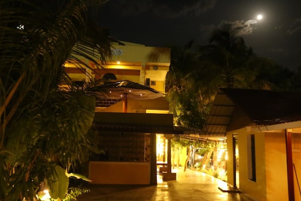 A building with a covered walkway, palm trees, and a moon in the sky.