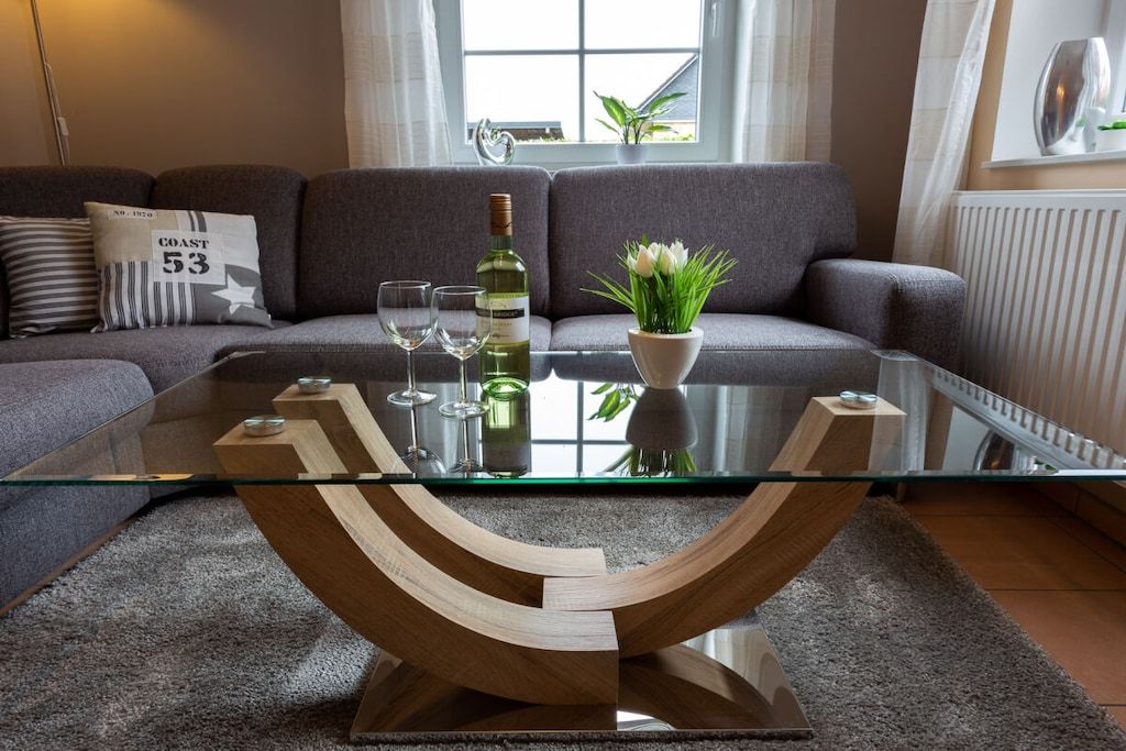 A modern living room with a glass coffee table, a bottle of wine, and a potted plant.