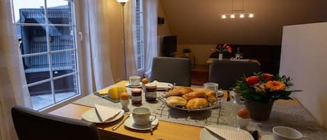 Ein Frühstückstisch für zwei Personen mit Croissants, Kaffee und einer Blumenkomposition.