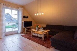 Un salon avec un canapé, une table basse, un téléviseur et une fenêtre avec des rideaux.
