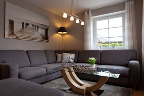 A modern living room with a glass coffee table, grey sofas, a painting, a lamp, and a window with curtains. - Baltic Sea holiday home II 300m to the beach (24398 Ostseebad Schönhagen)