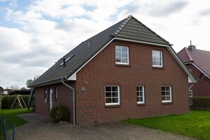 Une maison à deux étages, construite en briques, avec un toit en pente, une antenne parabolique et une allée pavée.