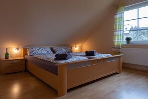 A bedroom with a sloped ceiling, a wooden bed, a nightstand with a bottle and glass, and a window with a view. - Baltic Sea holiday home II 300m to the beach (24398 Ostseebad Schönhagen)