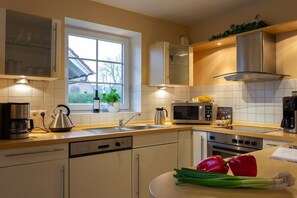 A modern kitchen with a dishwasher, stove, microwave, and a window with a view of a house. - Baltic Sea holiday home II 300m to the beach (24398 Ostseebad Schönhagen)
