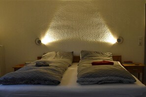 Un lit double avec une literie à motifs, deux tables de chevet et des lampes fixées au mur.