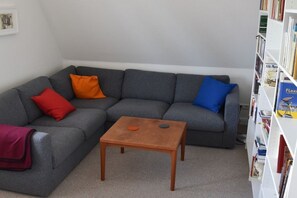 A living room with a grey sectional sofa, a small wooden coffee table, and a bookshelf filled with books. - Holiday apartment at the Baltic Sea resort (Flensburg)