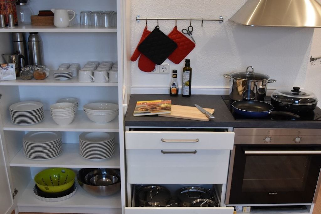 Une cuisine avec des armoires blanches, une cuisinière, des casseroles et divers ustensiles de cuisine.