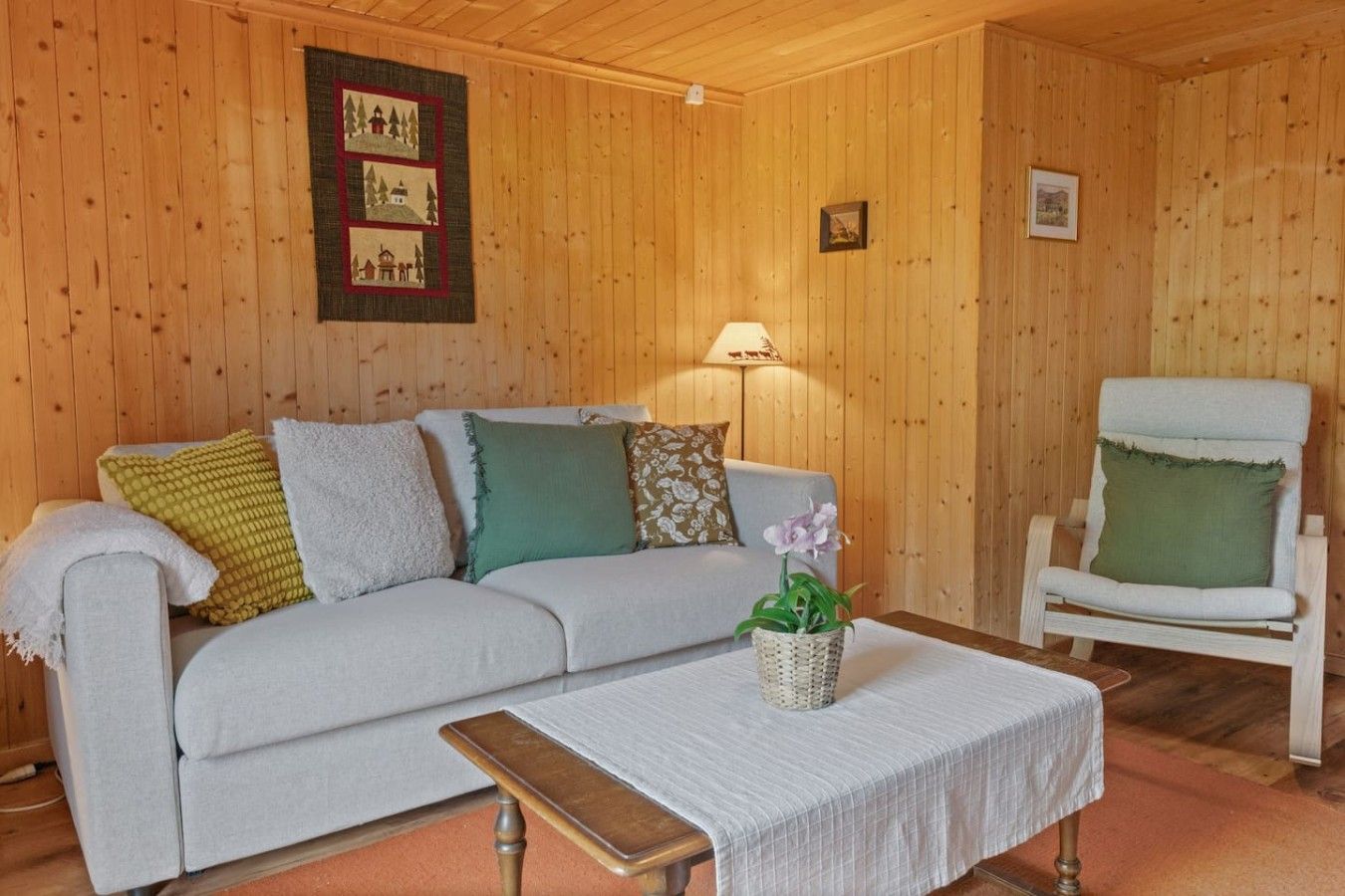 Une pièce confortable avec un canapé, un fauteuil, une table et une lampe.