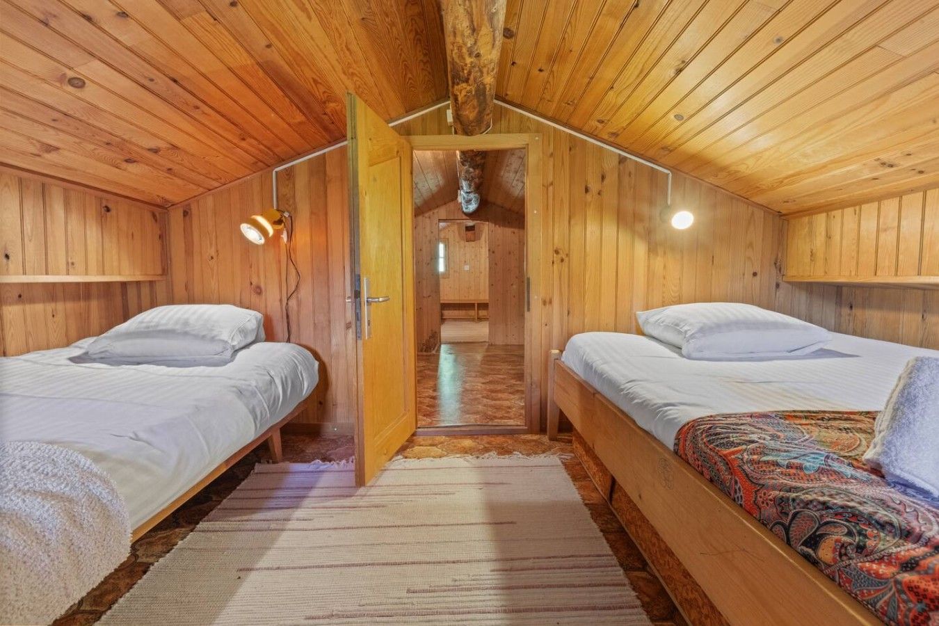 Une cabine avec deux lits superposés en bois, un plafond en bois et une porte visible donnant sur un couloir.
