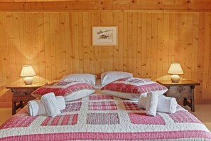 Une pièce aux murs lambrissés, comprenant un lit, deux tables de chevet et un tableau encadré accroché au mur.