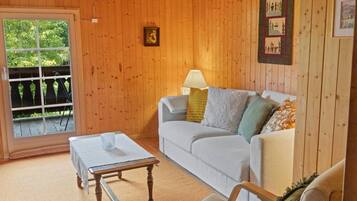 Ein gemütliches Zimmer mit einer Holzvertäfelung, einem weißen Sofa mit Kissen, einem kleinen Tisch und einem Fenster mit Blick auf Grünflächen.