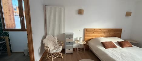 Un dormitorio con cabecera de madera, cama con dos almohadas, una silla, una mesita de noche con lámpara y un radiador.
