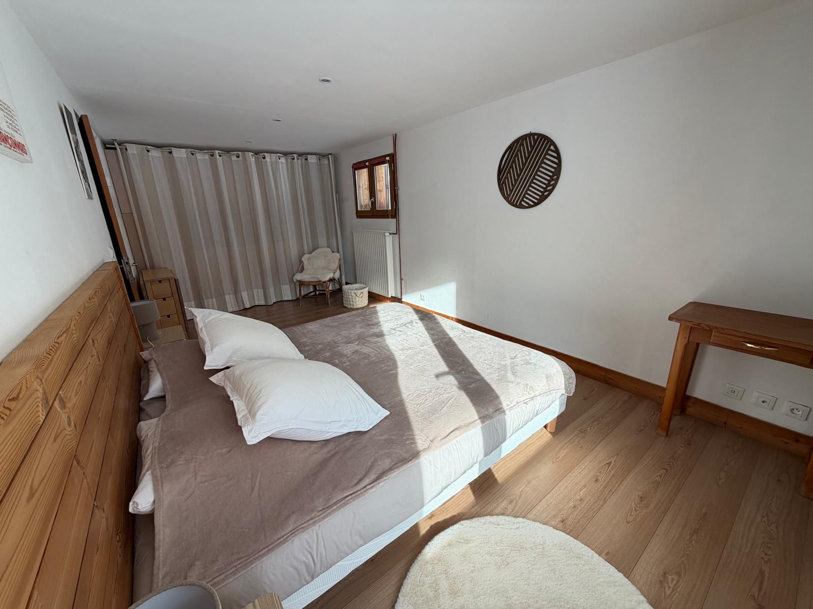A bedroom with a wooden bed, a bedside table, a chair, a radiator, and a window with curtains.