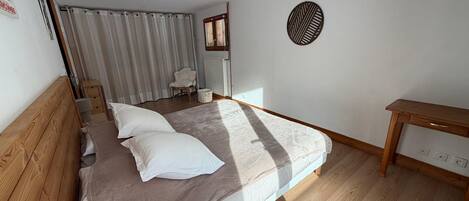 A bedroom with a wooden bed, a bedside table, a chair, a radiator, and a window with curtains.