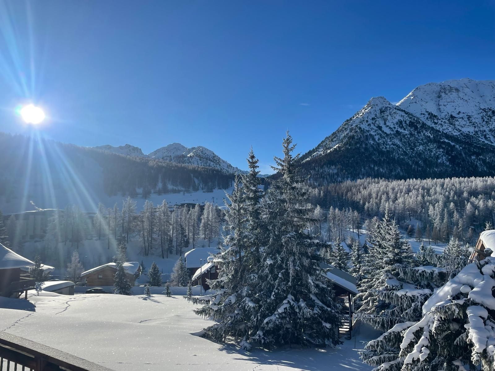 A snowy mountain landscape with a clear sky, a cabin, and a snow-covered tree.