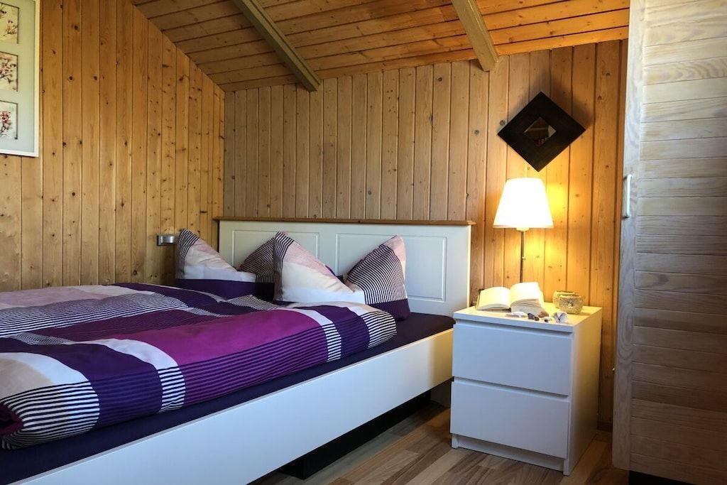 Une pièce aux murs lambrés, comprenant un lit, une table de chevet et une lampe fixée au mur.