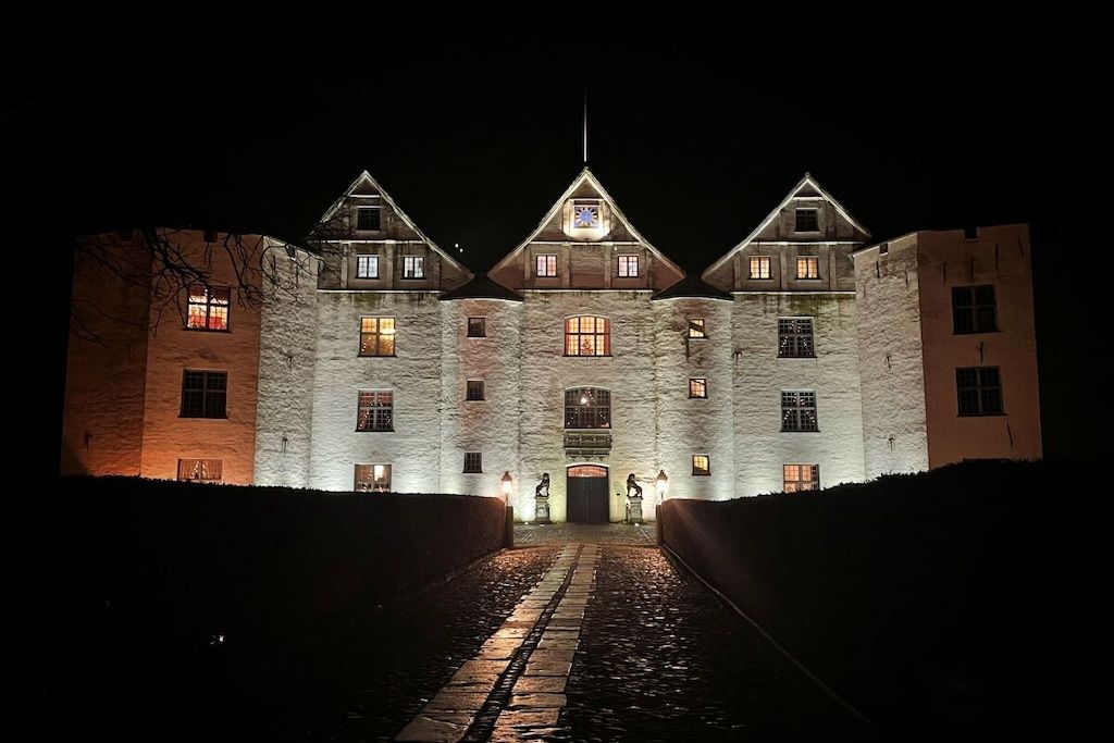 A large stone building with multiple windows and a central entrance, illuminated at night.