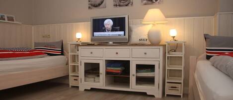 A bedroom with a bed, a TV, a nightstand, a lamp, and a cabinet.