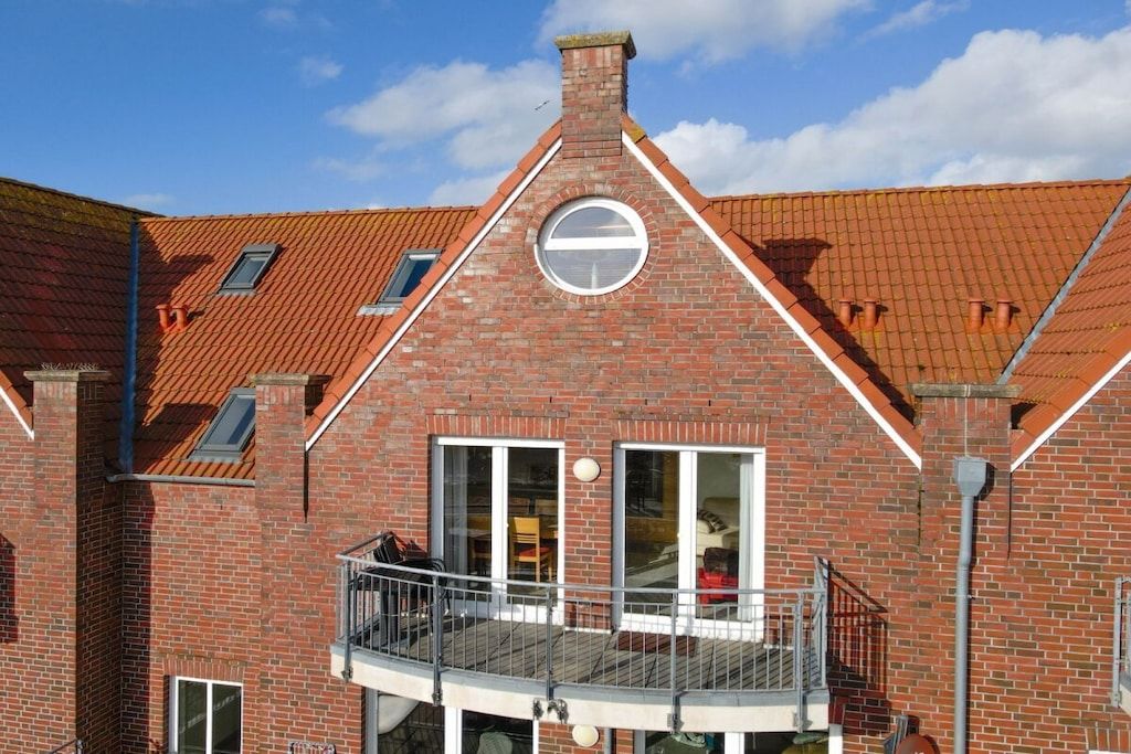 A red brick building with a balcony, large windows, and a chimney.