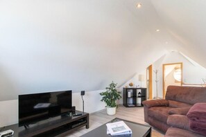 A modern living room with a flat-screen TV, a brown sofa, a coffee table, and a potted plant. - Holiday apartment with 1 bedroom (Norddeich)