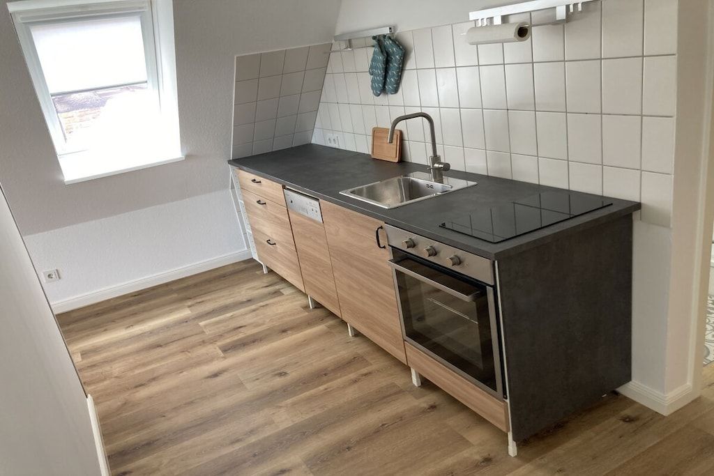 A kitchen with a dark countertop, wooden cabinets, a stainless steel sink, and a built-in oven.