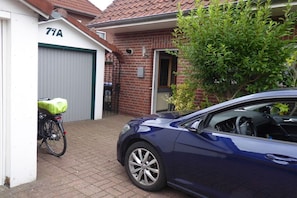 Ein Wohngebiet mit einem blauen Auto vor einem Haus, einem Fahrrad mit einer grünen Tasche und einer Garagentür mit der Nummer 71A.