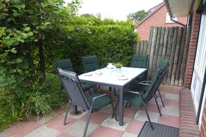 Een terras met een tafel en stoelen, omringd door groen en een houten hek.