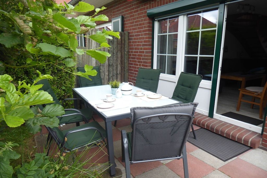 An outdoor patio with a table set for two, surrounded by chairs, and a brick wall in the background.