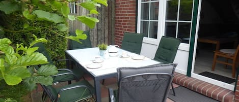 An outdoor patio with a table set for two, surrounded by chairs, and a brick wall in the background.