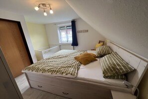 Ein Schlafzimmer mit einem Bett, einem Fenster mit Vorhängen, einem Heizkörper und einer Deckenleuchte.
