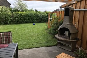 A backyard with a stone pizza oven, a wooden pergola, and a grassy lawn. - Holiday home with 3 bedrooms (Wangerland)