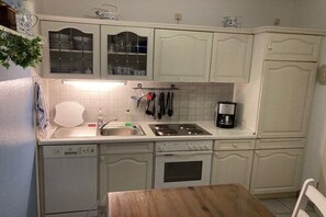A kitchen with white cabinets, a dishwasher, a stove, and a coffee maker. - Holiday home with 3 bedrooms (Wangerland)