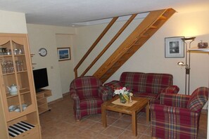 Ein Wohnzimmer mit einer Sofagarnitur, einem Fernseher, einer Holzkommode und einer Treppe.