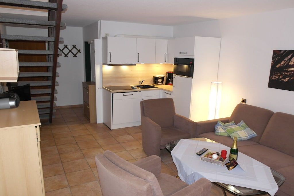 A compact living space with a kitchenette, a sofa set, and a dining table with a bottle of champagne.