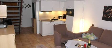 A compact living space with a kitchenette, a sofa set, and a dining table with a bottle of champagne.