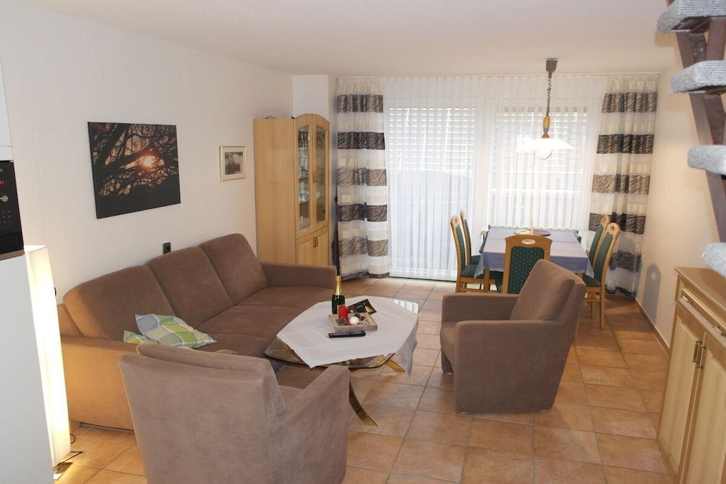 A living room with a sofa, armchairs, a coffee table, a dining table with chairs, a cabinet, and a painting on the wall.